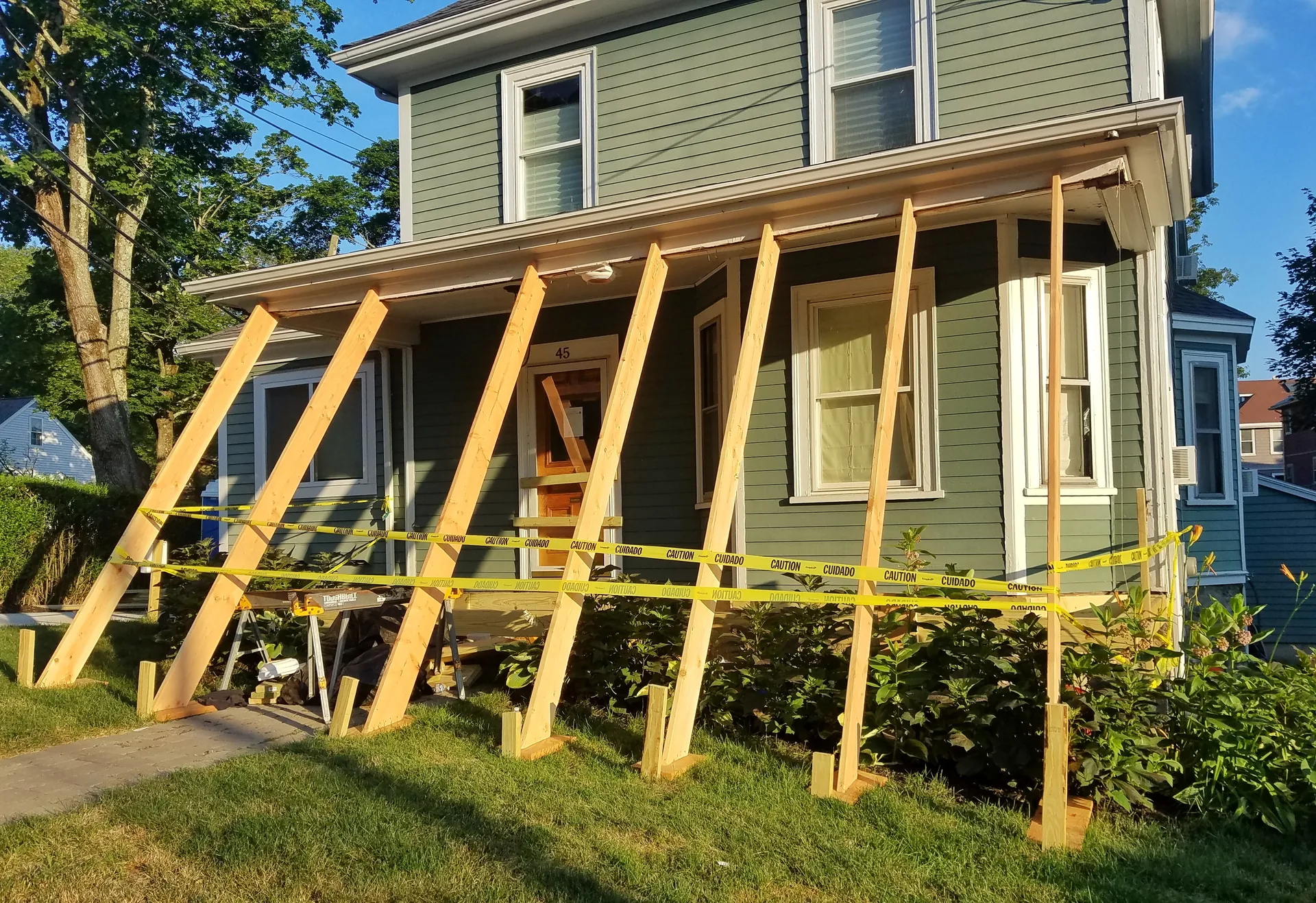 House porch mid-rebuild with angled shoring braces and caution tape